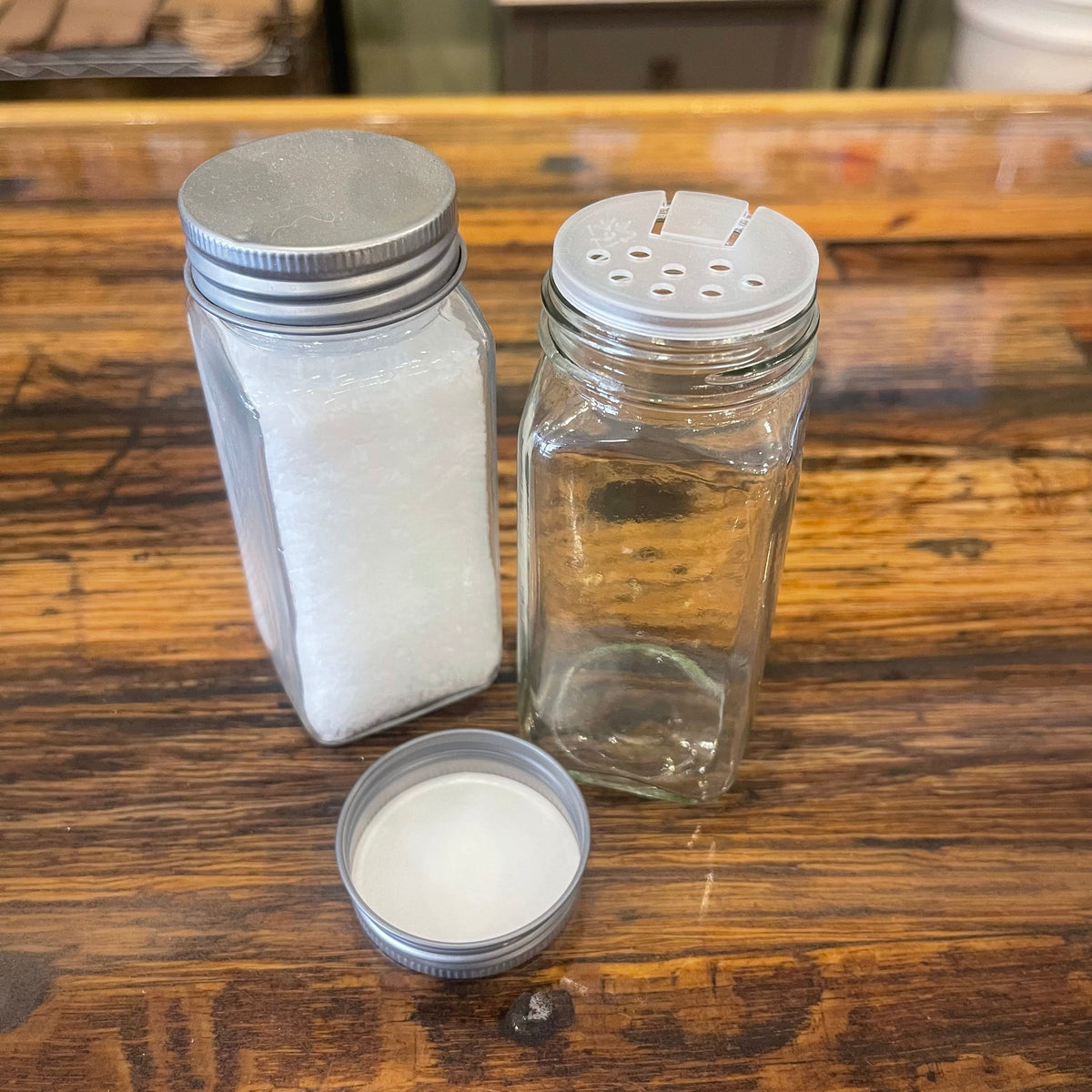 Clear glass spice jar with black lid, 4oz capacity, from OTB Refills, filled with colorful spices on a kitchen countertop.