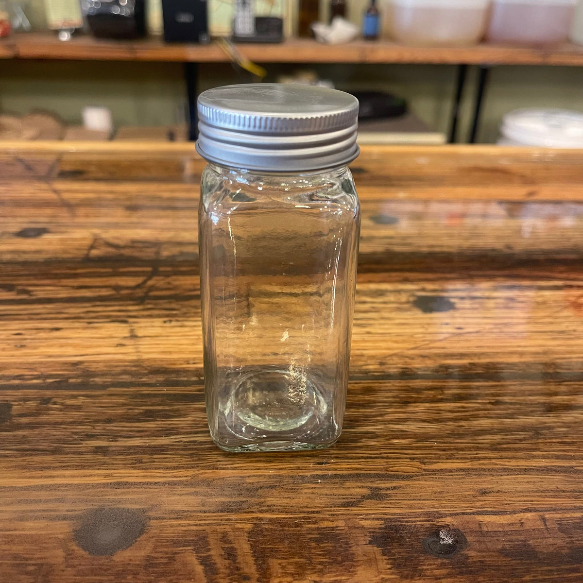 Clear 4oz glass spice jar from OTB Refills, showing a cylindrical container with a metal screw-on lid for storing spices.