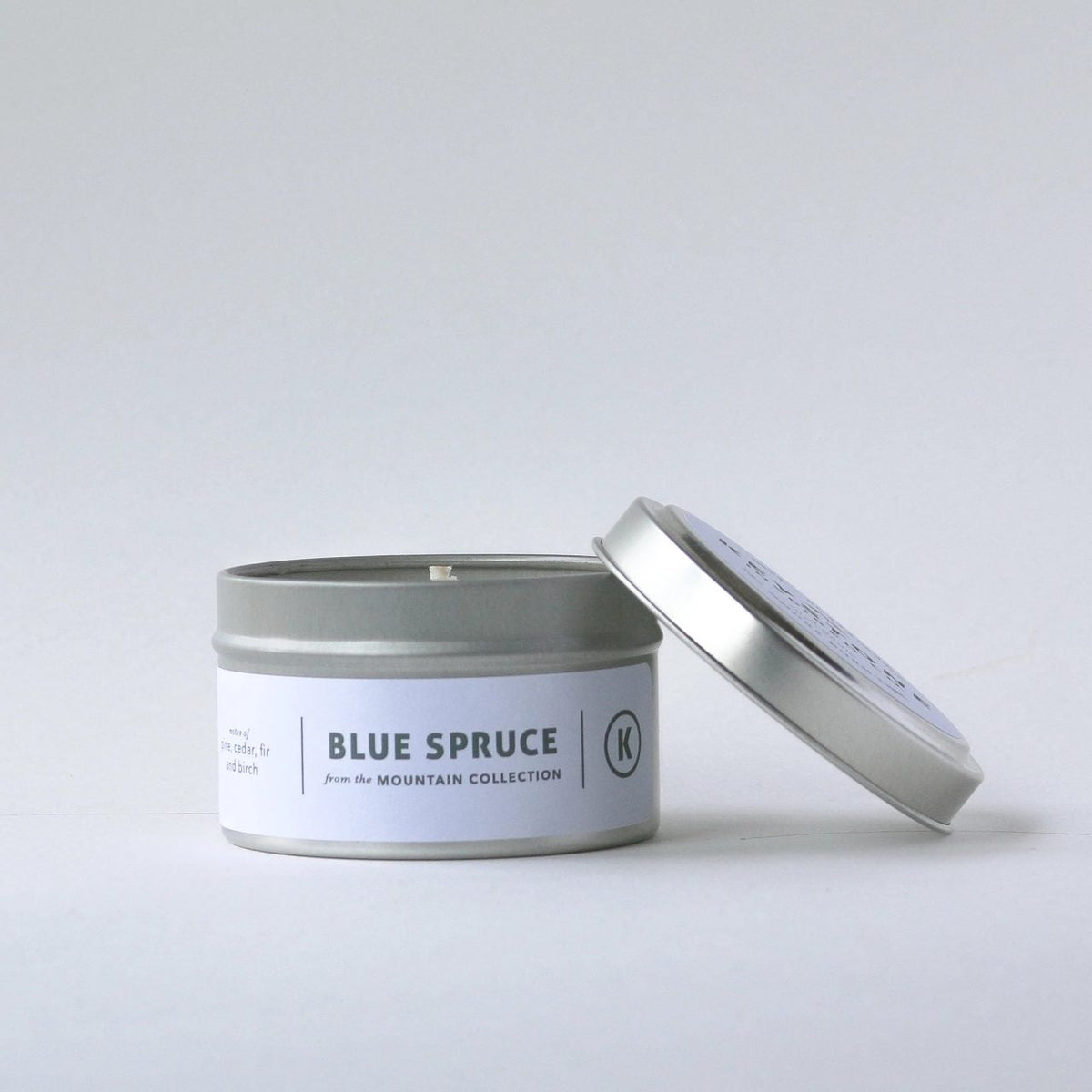 A 4 oz Keystone Inspired soy candle in a travel tin with a lit wick and minimalistic label, ideal for small space use.
