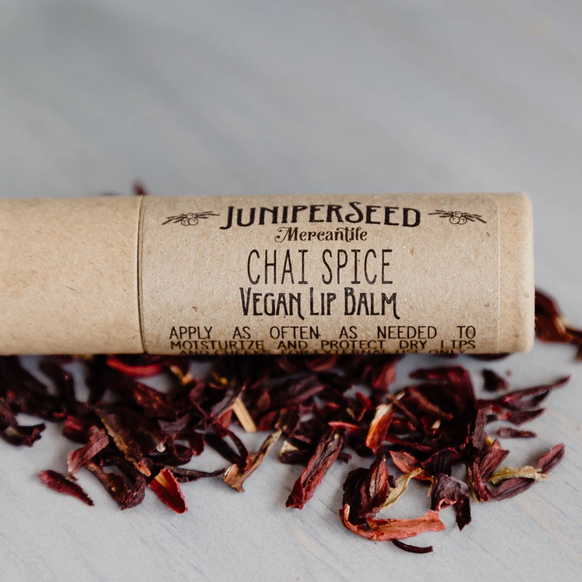 Juniperseed Mercantile Lip Balms in colorful tubes, displayed outdoors with natural sunlight highlighting the packaging.
